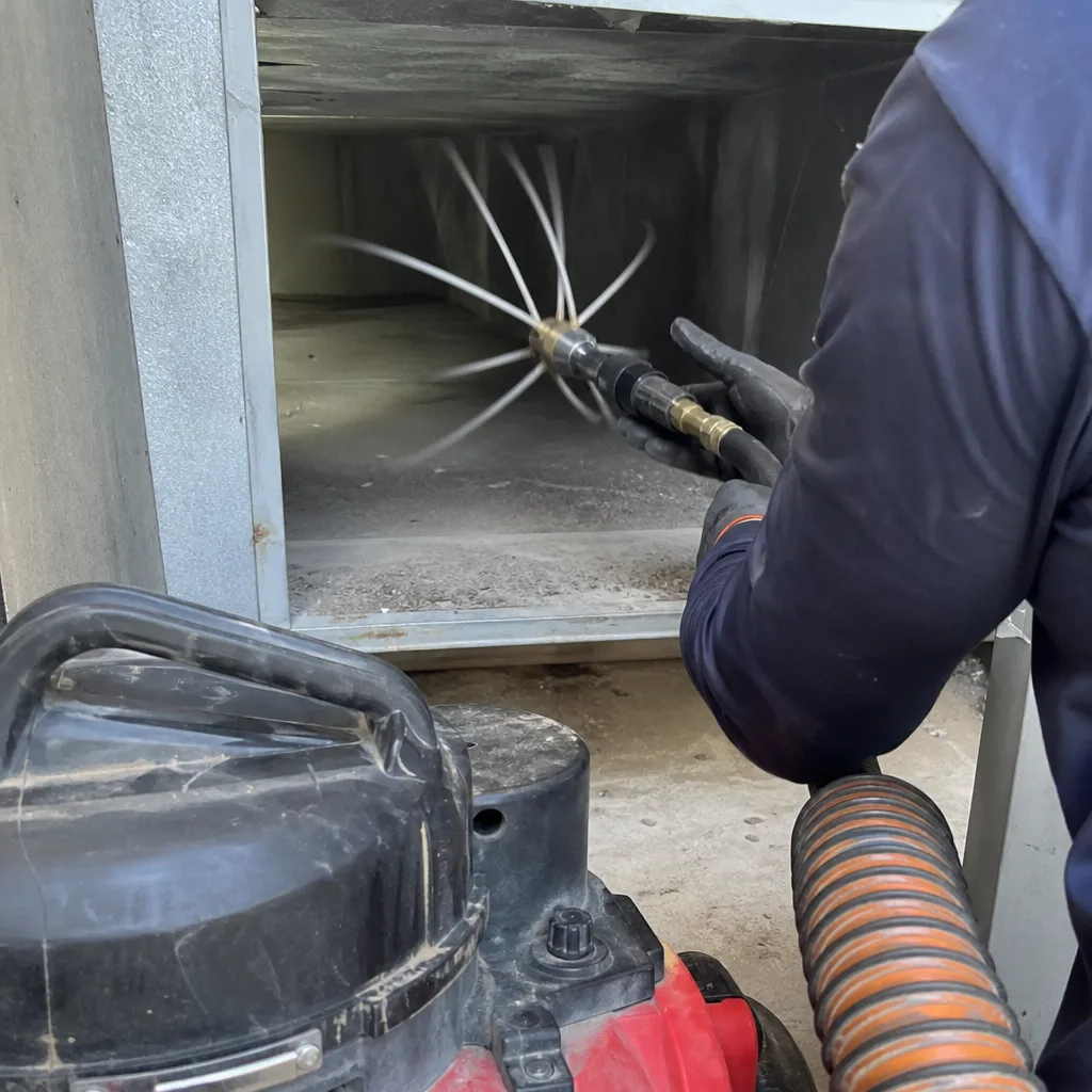 Technician using a rotating air duct cleaning tool inside ventilation shaft